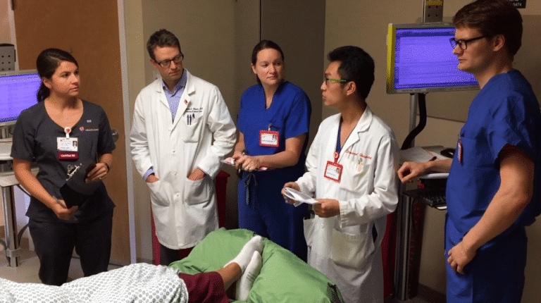 A doctor and group of health professions students visit a patient in the hospital